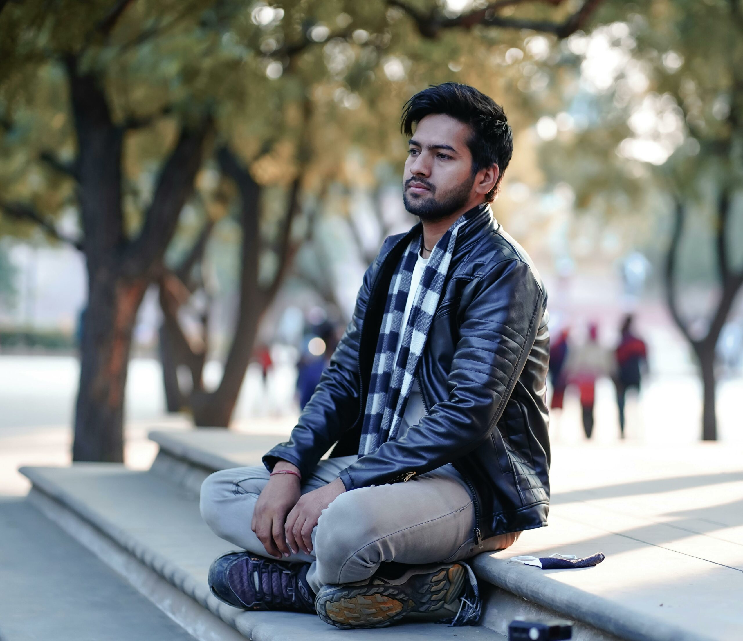 A contemplative young man name rahul jain sits on steps in Jaipur, wearing a leather jacket and scarf. He is client of Digital Marketing Specialist.