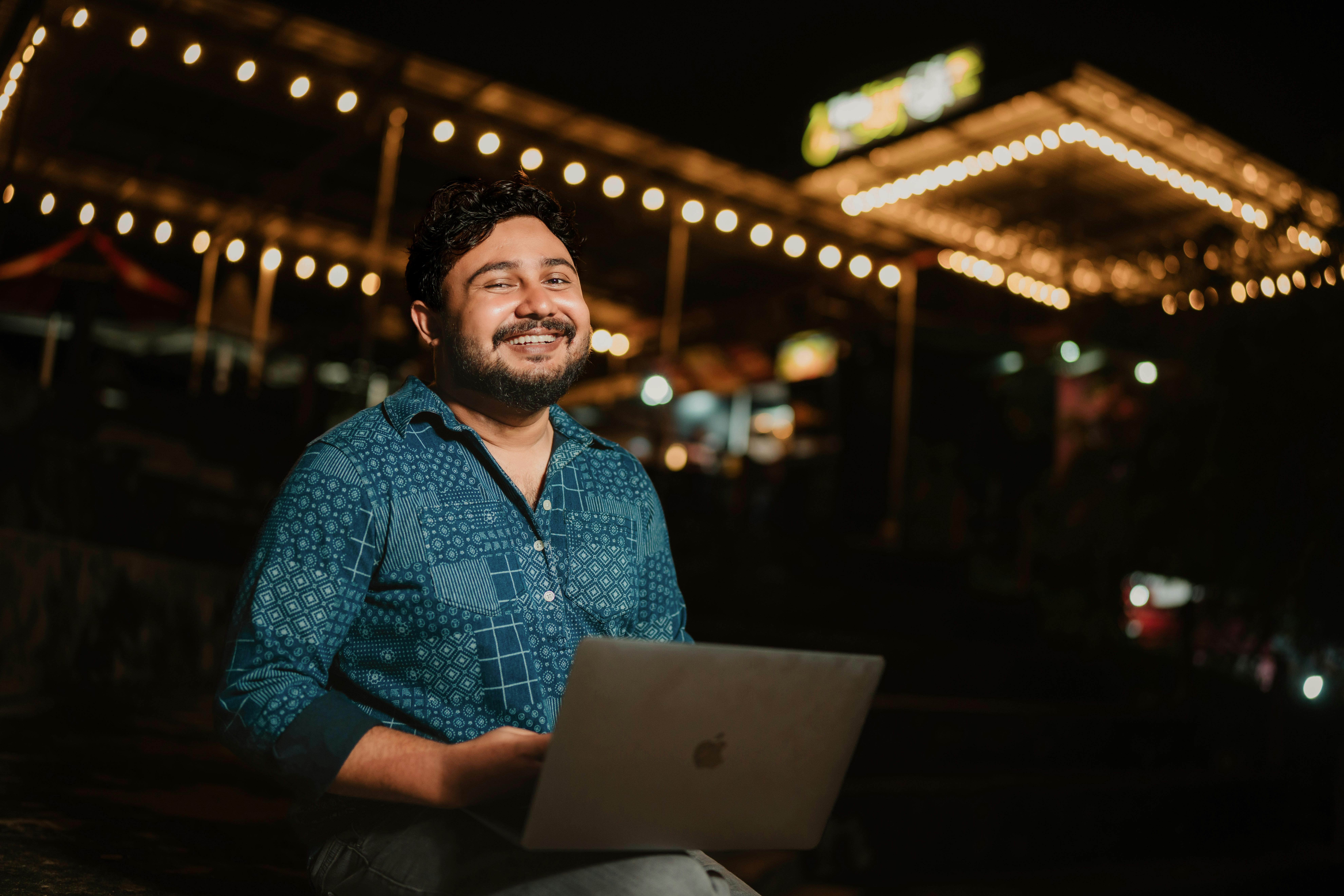 Cheerful man using laptop outdoors at night under festive lights. He is client of Digital Marketing Specialist named raj.