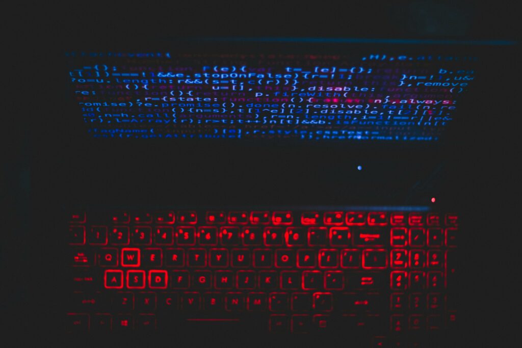 Dark-themed laptop setup with a red glowing keyboard and code on screen, ideal for tech enthusiasts.