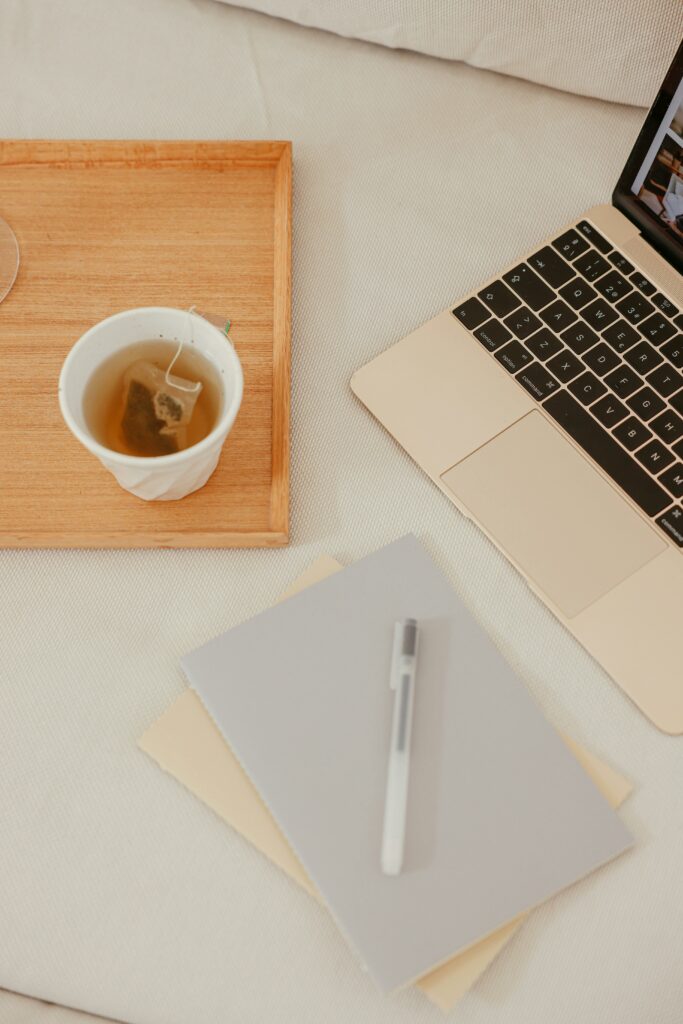 A tranquil workspace featuring a laptop, cup of tea, and notebooks on a wooden tray, ideal for productivity.