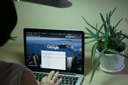 An adult browsing online using a laptop at a desk with a plant nearby, under soft lighting for Digital Marketing Services